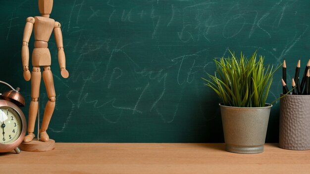 Empty space for product display on wooden tabletop with wood figure, alarm clock, plant and pencils over green blackboard. Study table concept