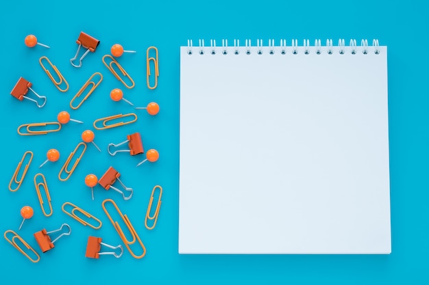 Empty spiral notebook and clips on blue background.