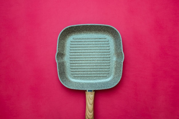 Empty square grill pan isolated on red background closeup, top view. Cooking concept backdrop with space for text