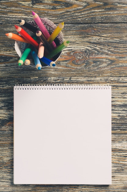 Empty square notebook and set of colorful pencils on the wooden table. Blank paper.