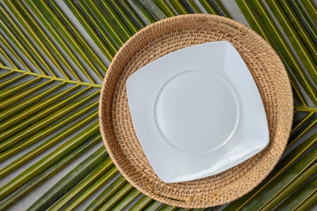 Empty square white plate in authentic wicker tray on green palm leaf