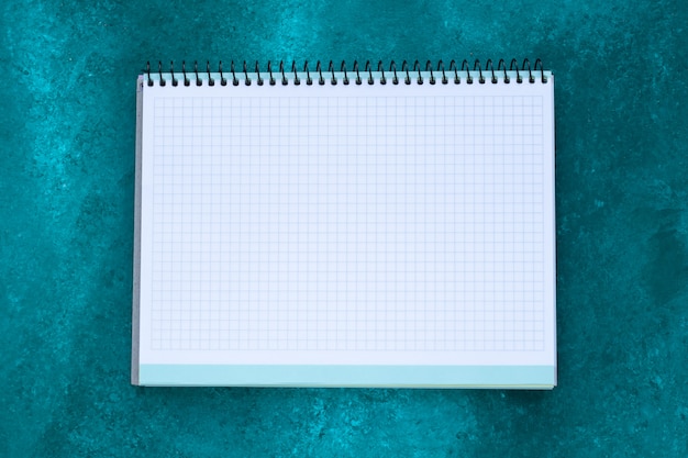 Empty squared notebook with copy space for text on abstract green painted background. Planning concept. White paper sheet.