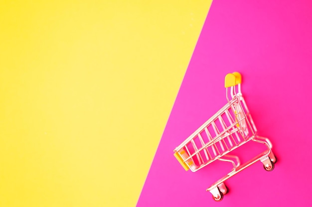 Empty stainless steel shopping cart isolated on pink and yellow background with copy space for your text or design. Top view, flat lay of shopping trolley. Supermarket, shopping, sale concept.