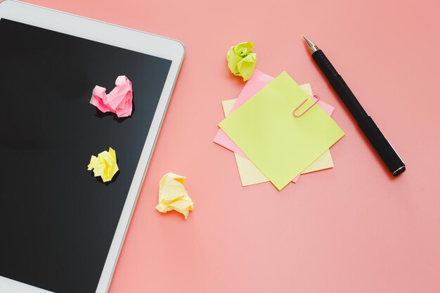 Empty sticky post note paper sheet and with digital tablet on pink table. workspace for text top view.