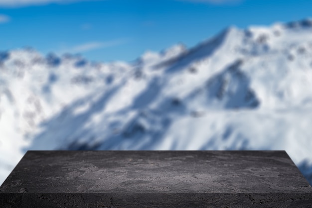 Empty stone surface on blurry background of snowy mountainous area on winter day and blue sky