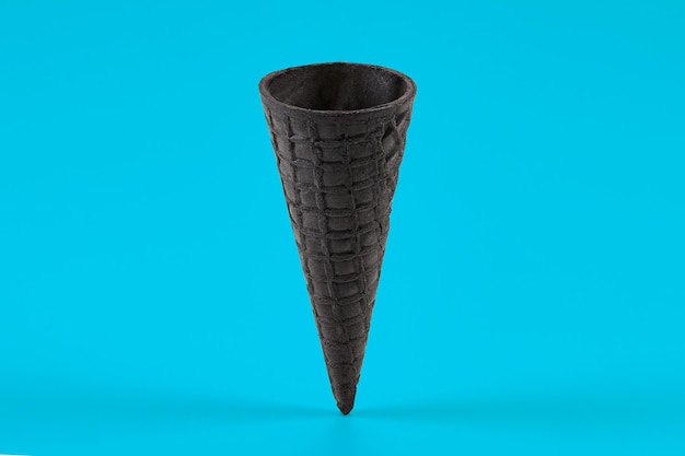 Photo empty sweet black wafer cone for ice cream on blue background concept of food treats mockup template