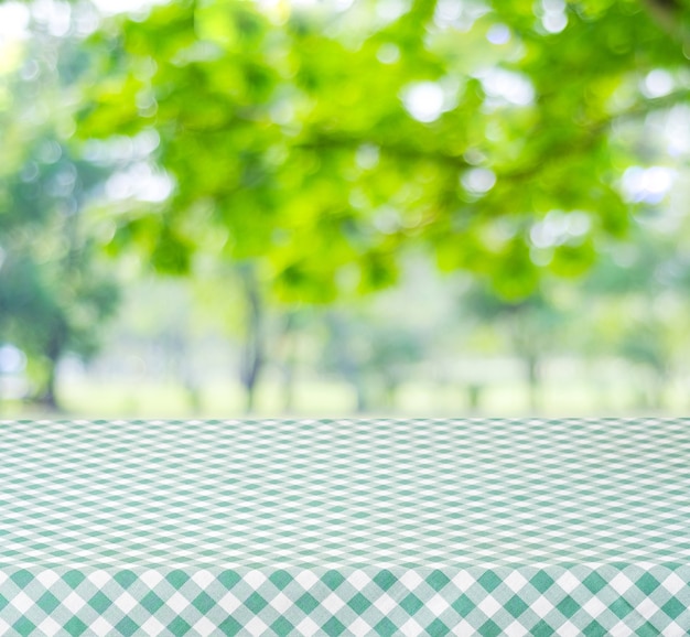 Empty table with green tablecloth over blur garden and bokeh background, for food and product display montage, spring and summer season