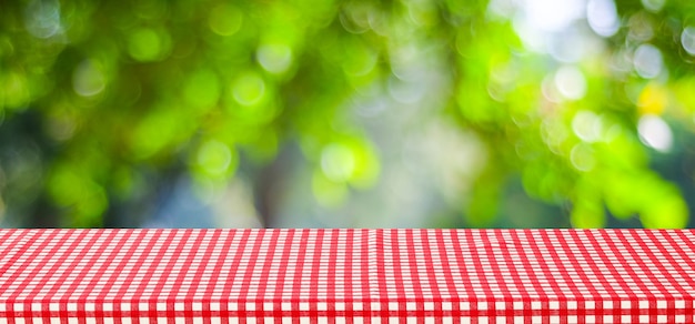 Empty table with red tablecloth over blur green tree and bokeh background, for food and product display montage background, banner