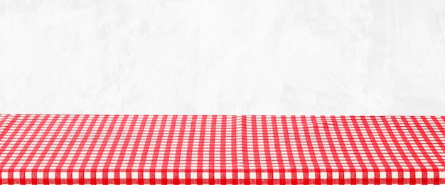 Empty table with red and white check pattern tablecloth over\
white wall background