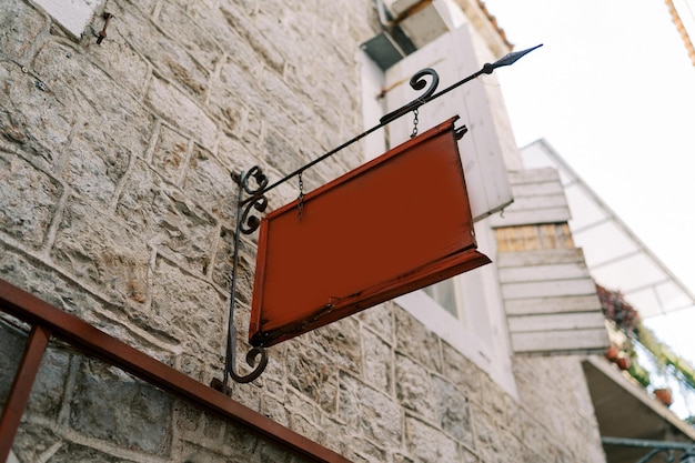 Photo empty tablet hangs on a forged signpost on the stone facade of an old house