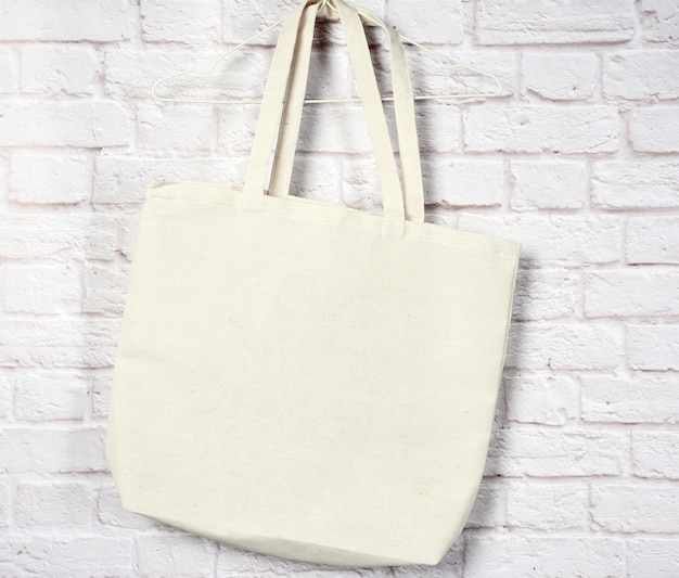 Empty textile eco bag hanging against a white brick wall, no\
plastic, zero waste