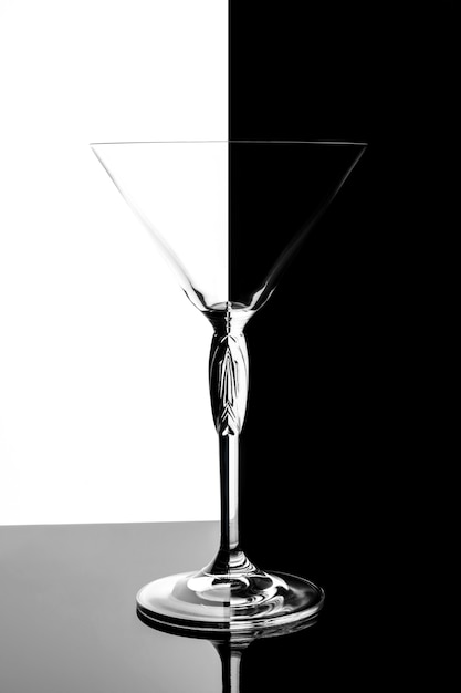 Empty transparent martini glass on black mirrored surface over black and , studio advertising shot, copy space