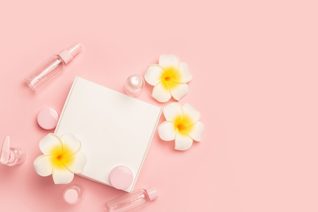 Empty tubes for cosmetics, flowers and gift box on a pastel pink surface