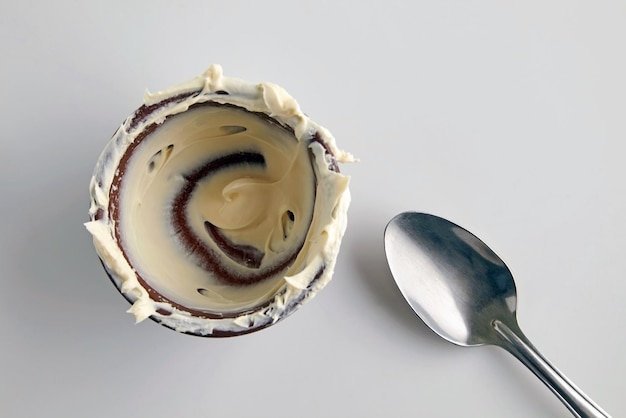 Пустая немытая миска с остатками еды и ложкой на белом фоне Остатки вкусного десерта кислого сливочного йогурта