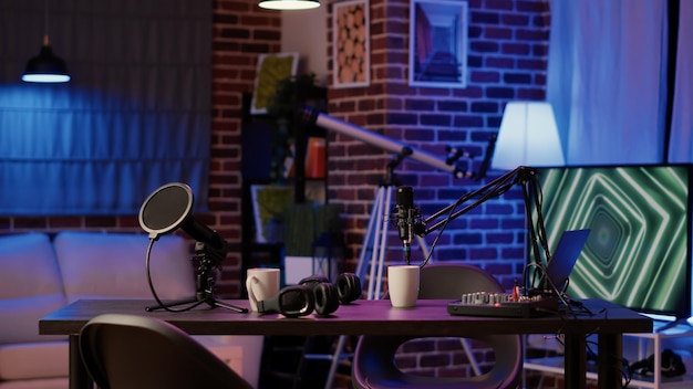 Empty vlogger desk with professional streaming equipment to broadcast live talk show on social media. Cozy ambient room with podcast station, microphone and headphones, sound production.