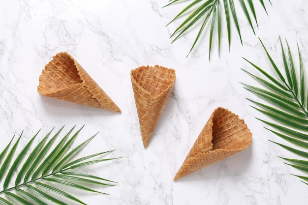 Empty waffle cones on marble background with palm leaves