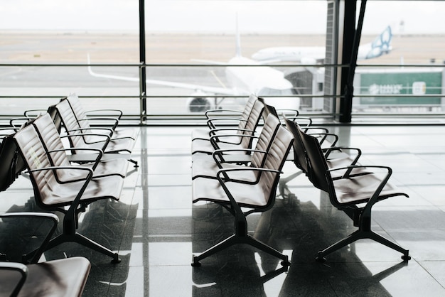 국제 공항의 빈 대기실 측면에서 비행기 선택적인 초점이 있는 창 배경에 좌석 의자가 줄지어 있는 모습