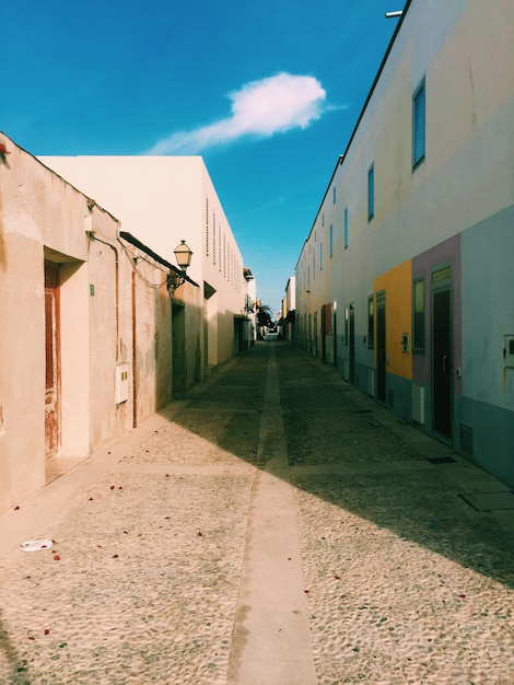 Empty walkway amidst houses against blue sky on sunny day