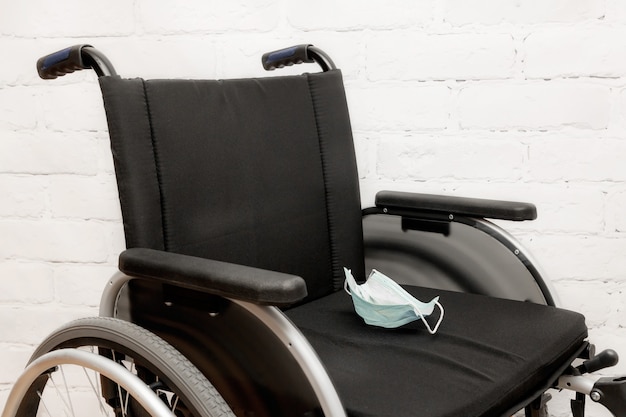 Foto una sedia a rotelle vuota con una maschera medica usata contro un muro di mattoni