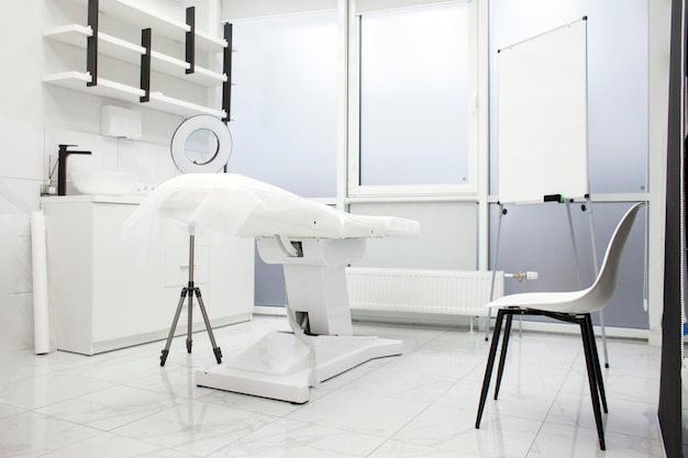 Пустой белый медицинский кабинет косметолога с современным косметологическим оборудованием и креслом