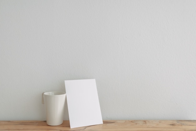 Empty white card mockup lean on a tea cup with white wall