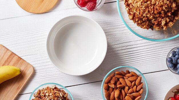 Empty white ceramic bowl on a white table with natural ingredients for preparing delicious healthy organic breakfast. Concept of healthy eating.