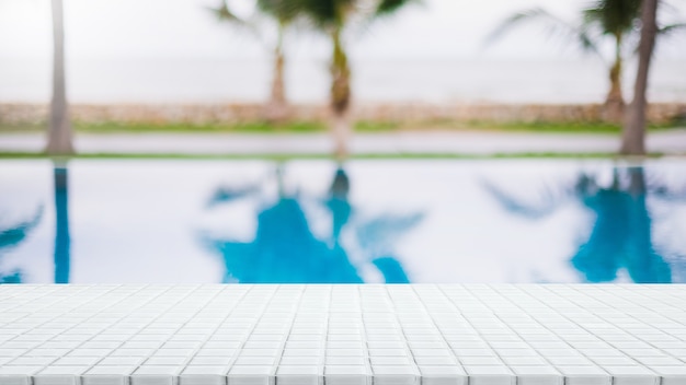Empty white ceramic mosaic table top and blurred swimming pool in tropical resort