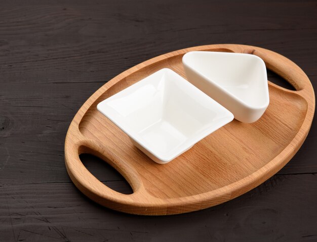 Empty white ceramic plates and oval wooden tray board on a wooden background, top view