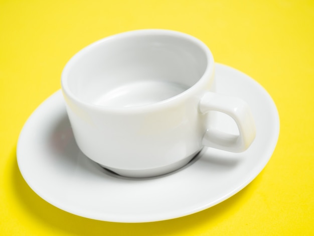 Photo an empty white cup and saucer on a yellow background, a copy of the space