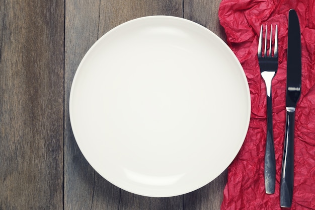 Empty white dish with Silver fork and spoon on red paper art on wooden floor.