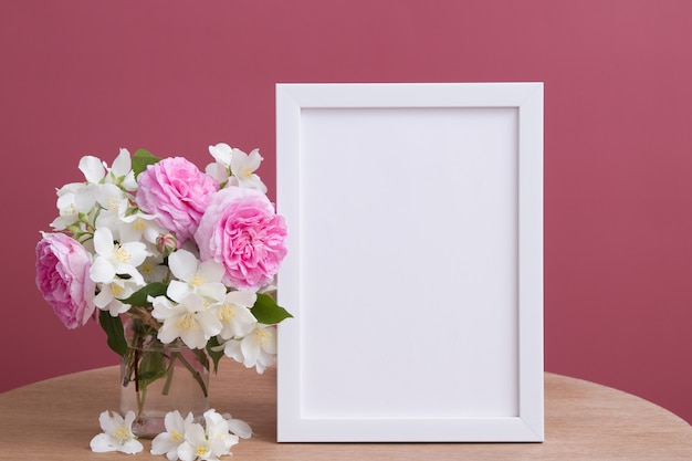 Empty white frame mock up with flowers on pink background.\
temlate for your text or picture