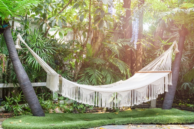 Empty white hammock hanging between palm trees in the garden 