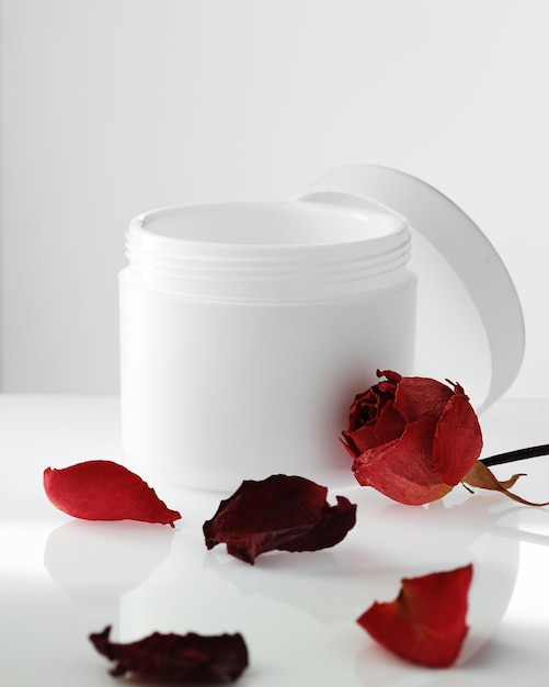 Vaso di plastica bianco vuoto con coperchio aperto su sfondo chiaro petali di rose rosse cosmetici ringiovanenti