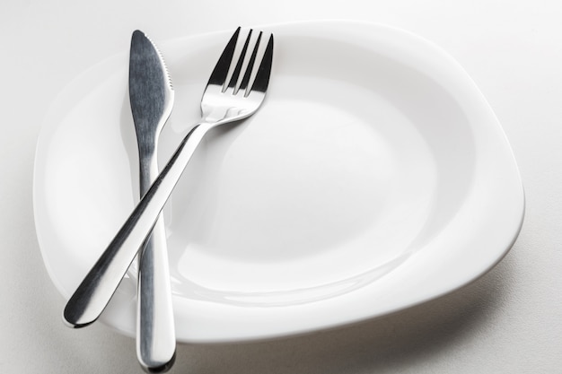 Empty white plate, fork and knife on a white background.