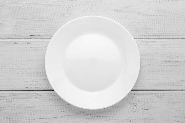 Empty white plate on gray wooden table. Top view. Wood board background.