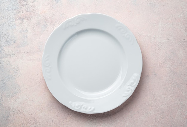 An empty white plate on a light pink background. Top view, horizontal.