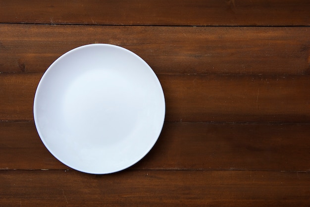 An empty white plate placed on a wooden floor