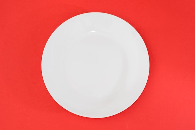 Empty white plate on a red background. View from above.