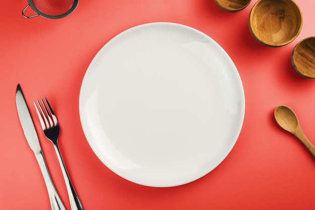 Empty white plate on the red table Top view Kitchen utensils beside like fork knife bamboo containers