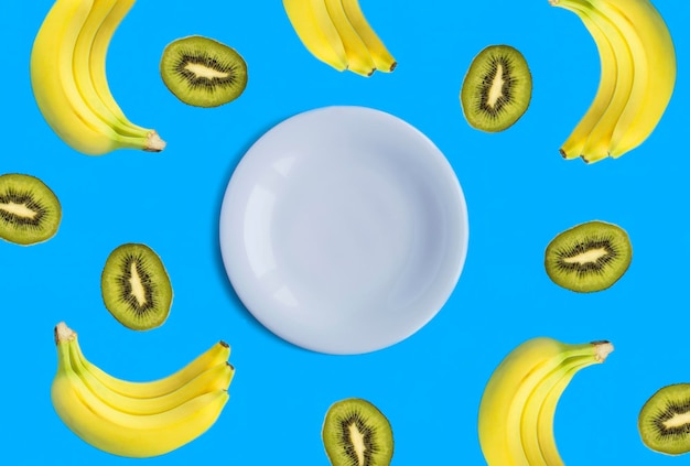 Empty white plate for text banana and kiwi on the blue background Top view Copy space