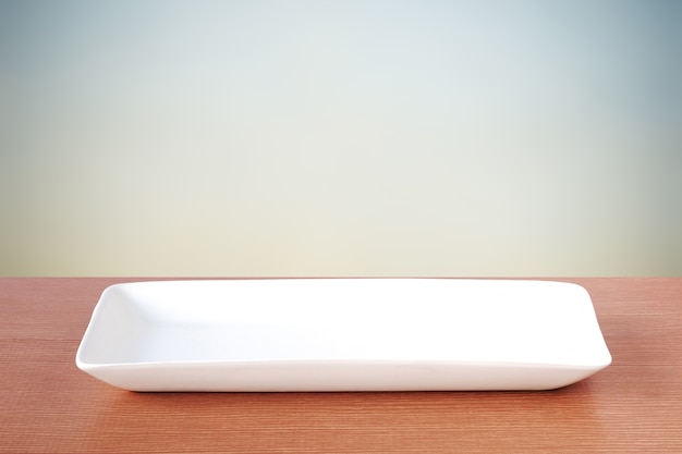 Empty white plate on wood table over blue cement wall background