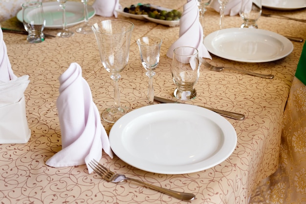 Photo empty white plates with napkins, vineglasses,  forks, knives, closeup, cutlery on the banquet table in restaurant