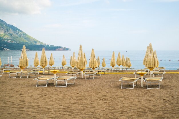 Empty white sun loungers without people under umbrellason the pebble beach by the sea