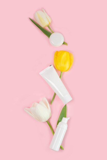 Empty white tubes and bottles with white tulips on a pink surface flat lay copy space