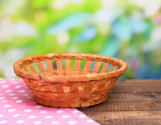 Empty wicker basket on wooden table on bright background