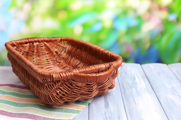 empty wicker basket on wooden table on bright background