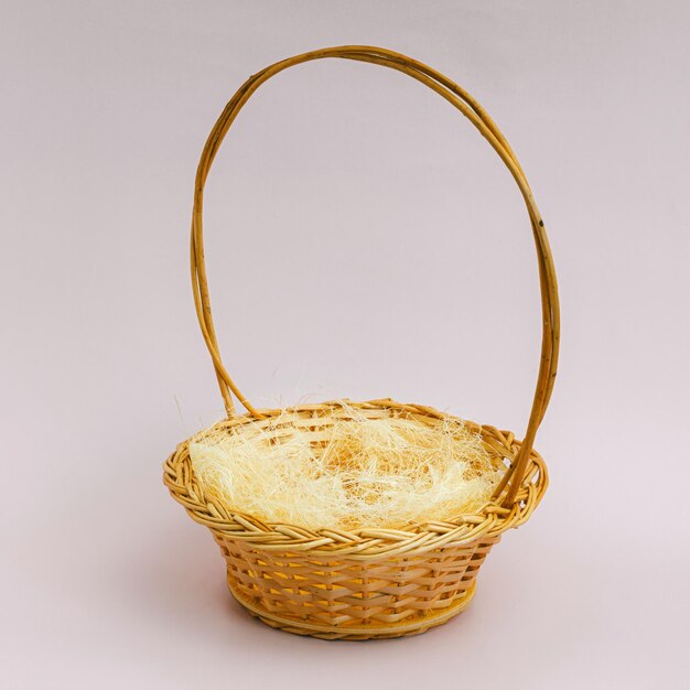 An empty wicker basket of yellow color with a round handle stands on a light background Blank for layout