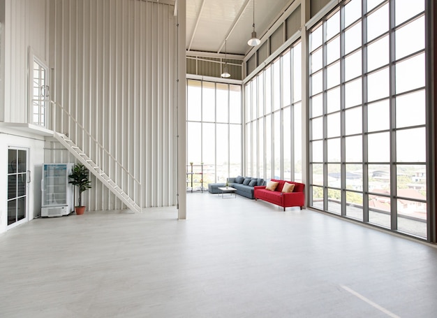 Empty wide and tall indoor industrial design photography studio workshop living room full of space with red and gray sofa set with wood table near glass windows with small office inside.