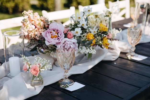 야외에서 모란과 장미로 만든 꽃 중앙 장식품 옆 테이블에 빈 와인 잔