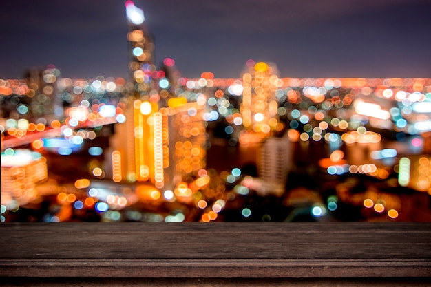 Empty wood table on soft bokeh of light night city background, counter can be placed your produce 